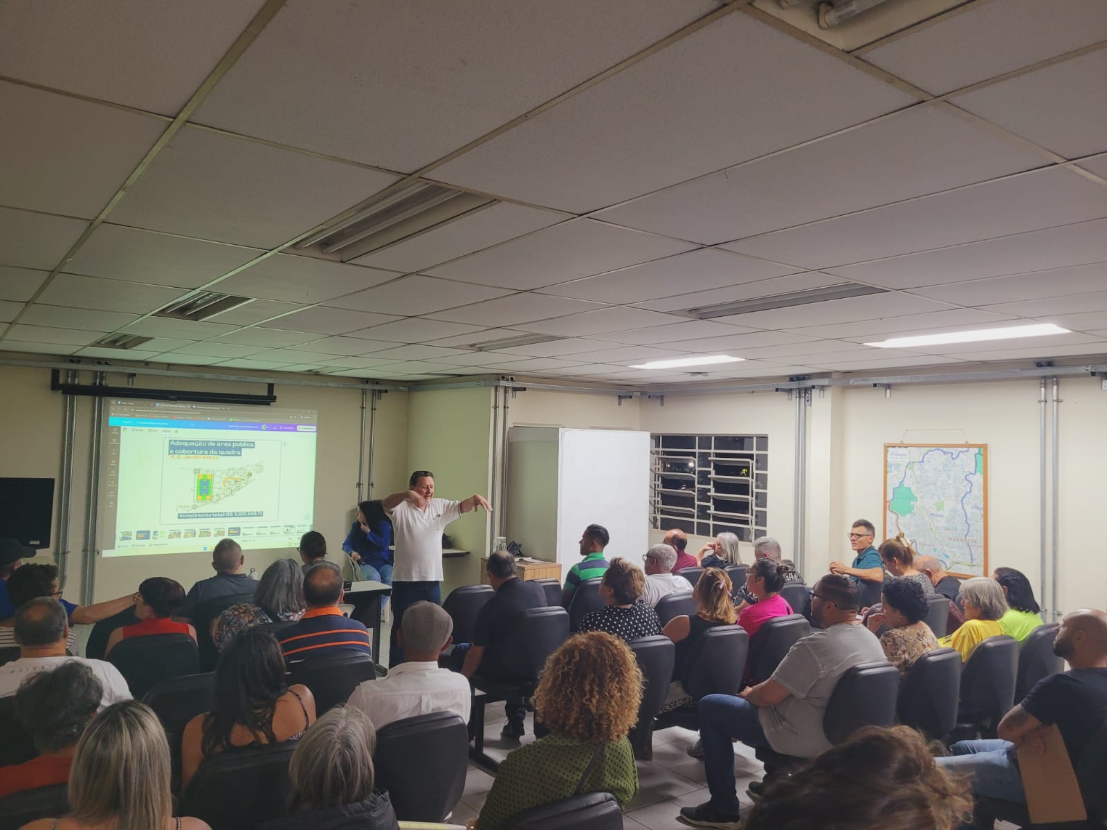 Foto da reunião tirada de trás, com pessoas sentadas e o Subprefeito na frente 